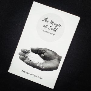 black background with a white zine that has a hand holding a pile of salt