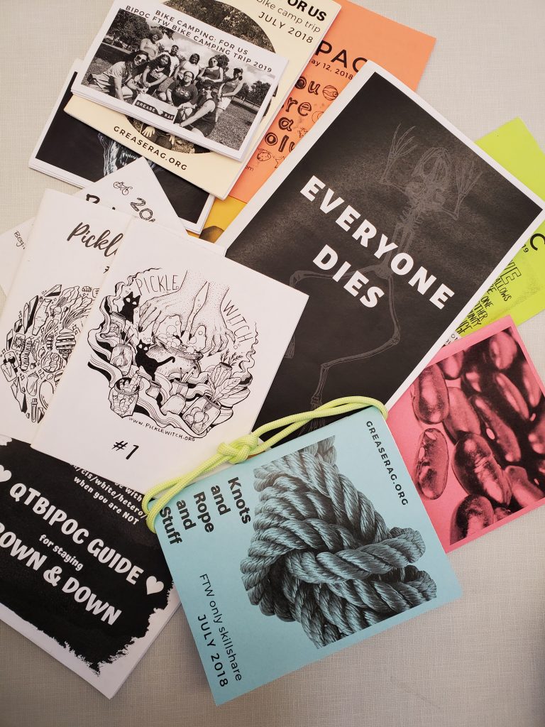 assortment of zines laid out on a white table in a pile