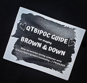 zine cover is at an angle on a black background, with a black shape with white text