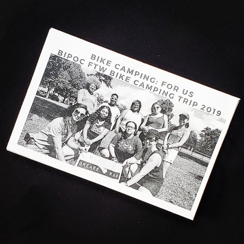 zine cover is at an angle on a black background, with a group photo of people standing and kneeling